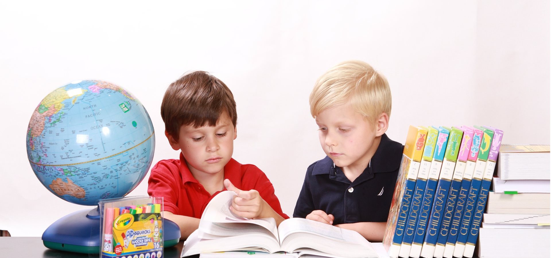 Two children sitting at a desk looking through some books
