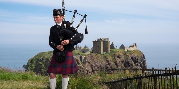 A piper playing the bagpipes with a castle in the background