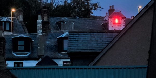 The rooftops of a town at night with a red light shining through a window
